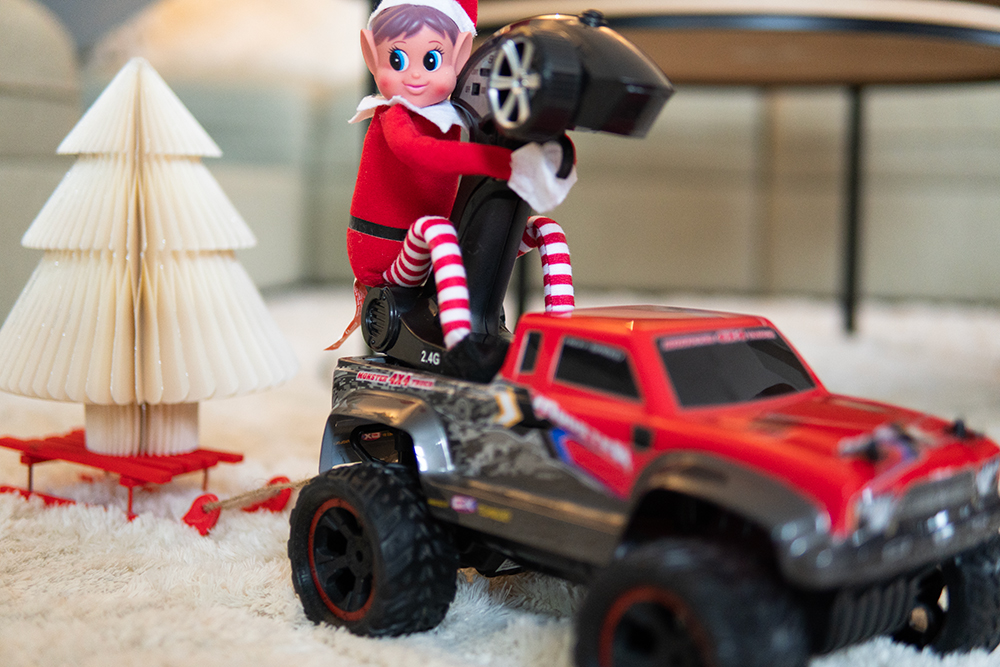 Rampenissen sitter på en radiostyrt bil med kjelke som henger fast, oppå kjelken står et pyntejuletre